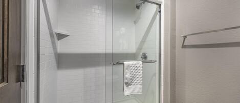 Une douche fermée par des parois de verre, avec des murs recouverts de carreaux blancs et une serviette blanche suspendue à un porte-serviettes en métal.