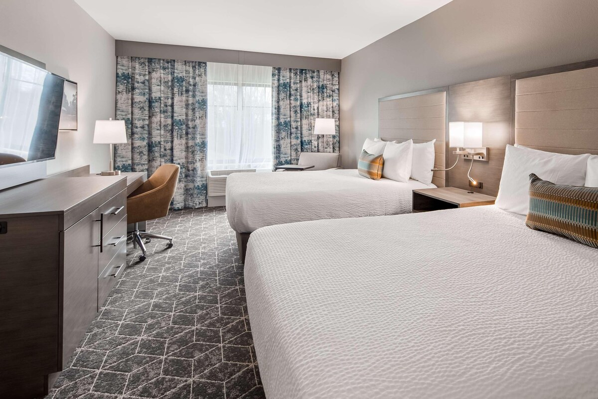 A hotel room with two beds, a desk, a chair, and a television.