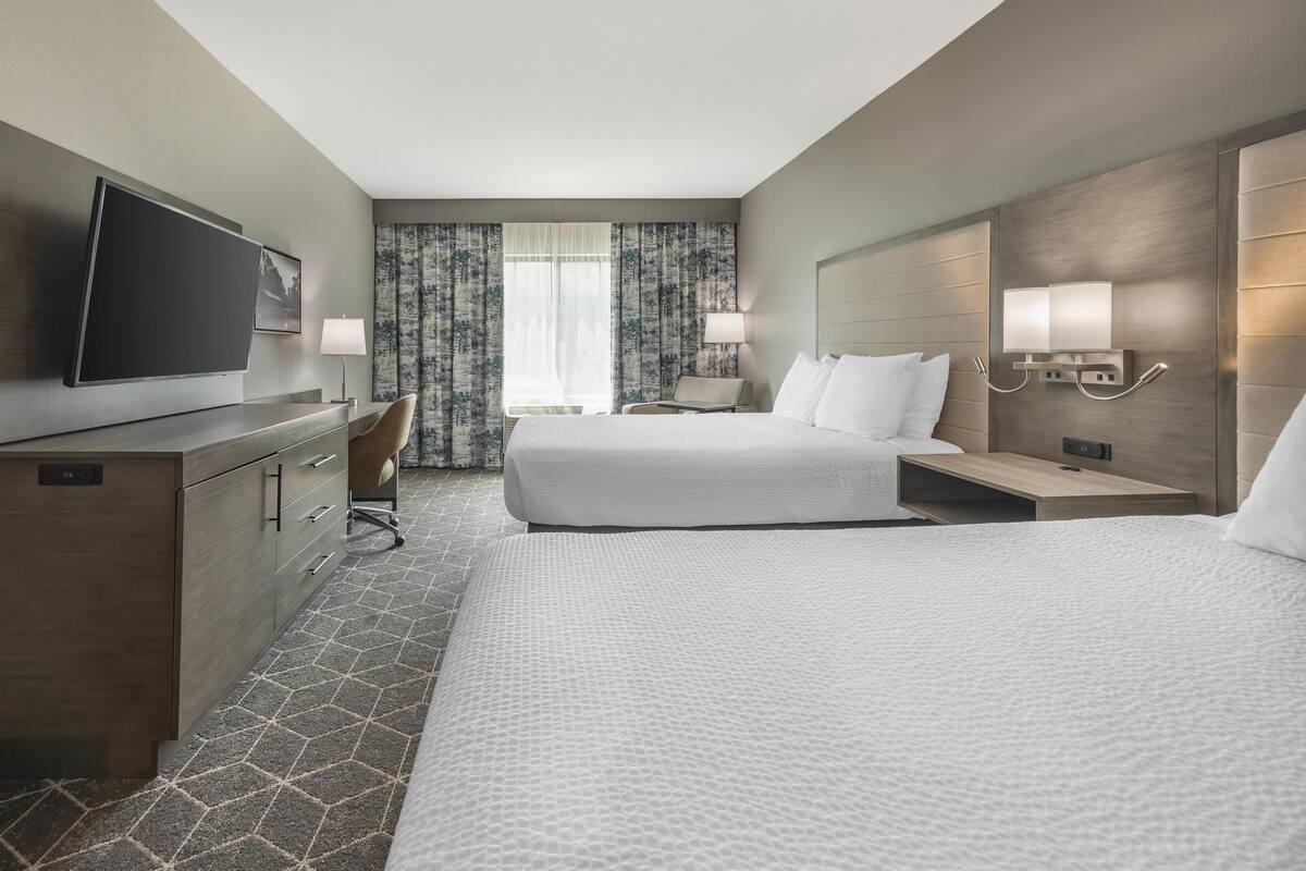 A hotel room with a large bed, a desk with a chair, a television, and a window with curtains.