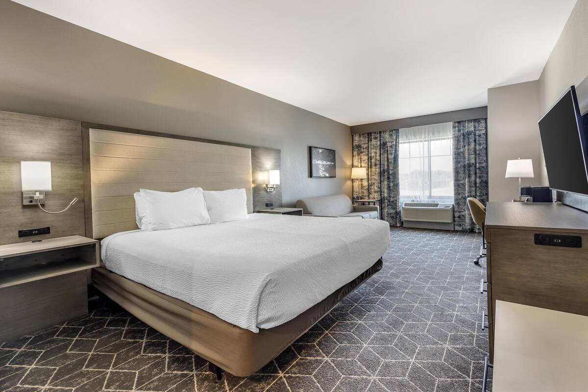 A hotel room with a large bed, bedside tables, a desk, and a television.