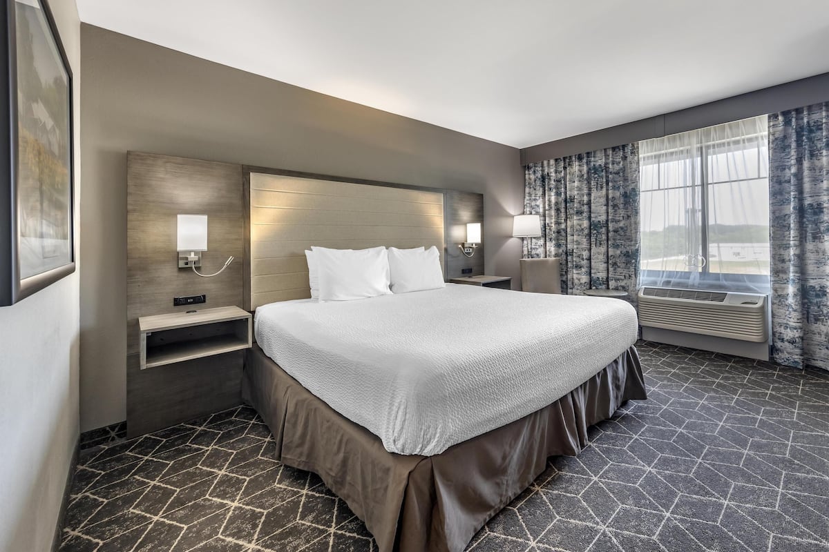 A hotel room with a large bed, bedside tables, a wall-mounted TV, and a window with curtains.
