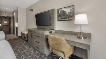 A hotel room with a bed, a desk with a chair, a TV, a lamp, and a framed picture on the wall.