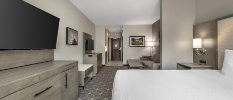 A modern hotel room with a large bed, a flat-screen TV, a desk, and a chair.