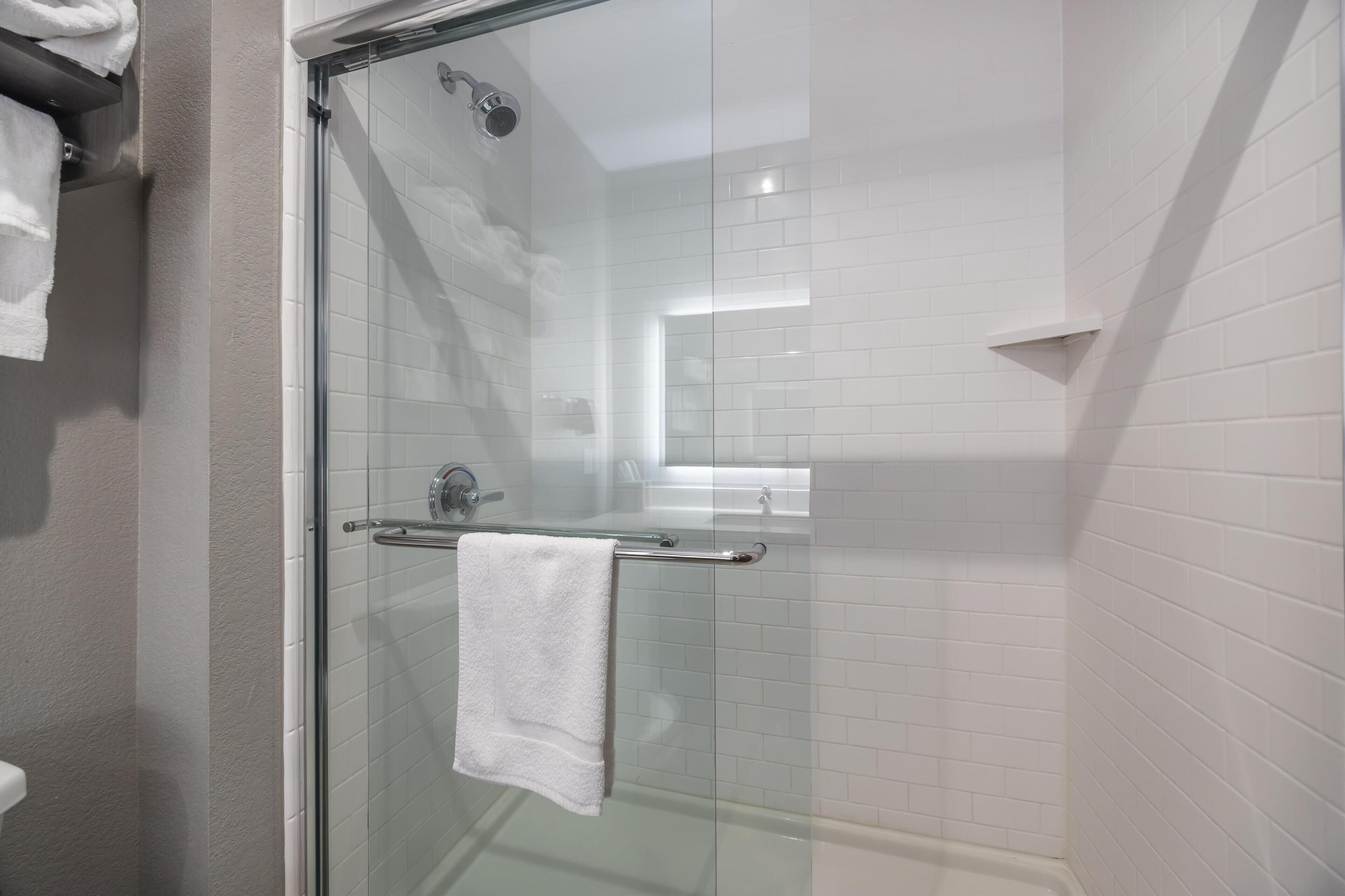 Une salle de bain moderne avec une douche à parois de verre, une serviette blanche suspendue à un porte-serviettes en métal et des murs recouverts de carreaux blancs.