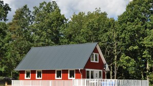 A red cabin with a white porch and a metal roof, surrounded by trees.