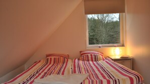 A bedroom with a single bed, striped bedding, a bedside table with a lamp, and a window with a view of trees.