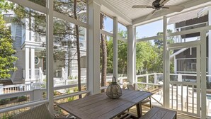 A covered outdoor area with a wooden table and benches, large windows, and a ceiling fan. - WaterSound Retreat w/ Pool and Golf Cart (Panama City Beach)