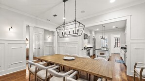 A spacious dining area with a wooden table and upholstered chairs, a hanging light fixture, and white cabinetry. - WaterSound Retreat w/ Pool and Golf Cart (Panama City Beach)