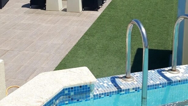 Un espace piscine avec vue sur l’océan, un coin salon avec des chaises et une table, et un bord de piscine revêtu de carreaux.