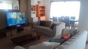 Un salon comprenant un téléviseur, un canapé, une table basse et un coin repas avec des chaises et une table.