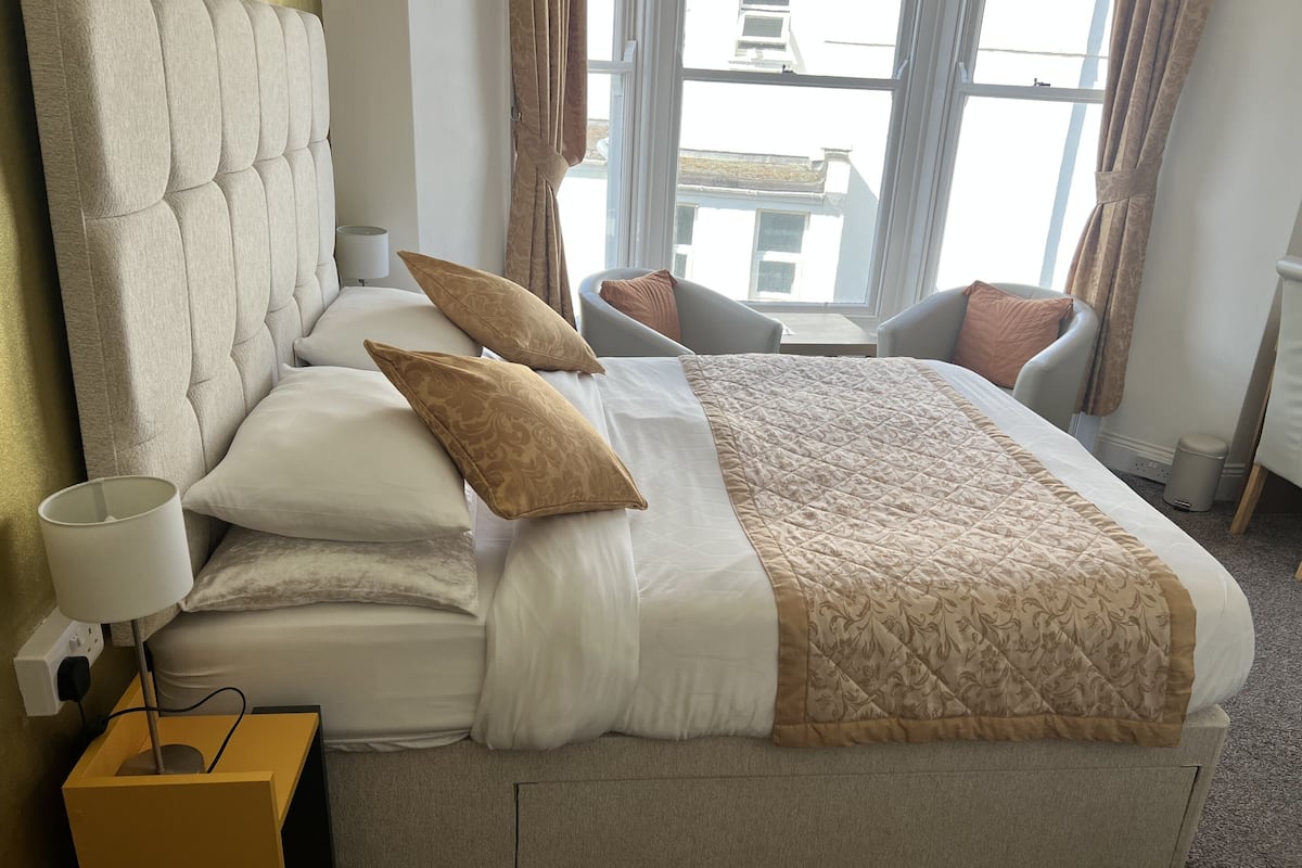 A neatly made bed with a headboard, multiple pillows, and a bedside lamp.