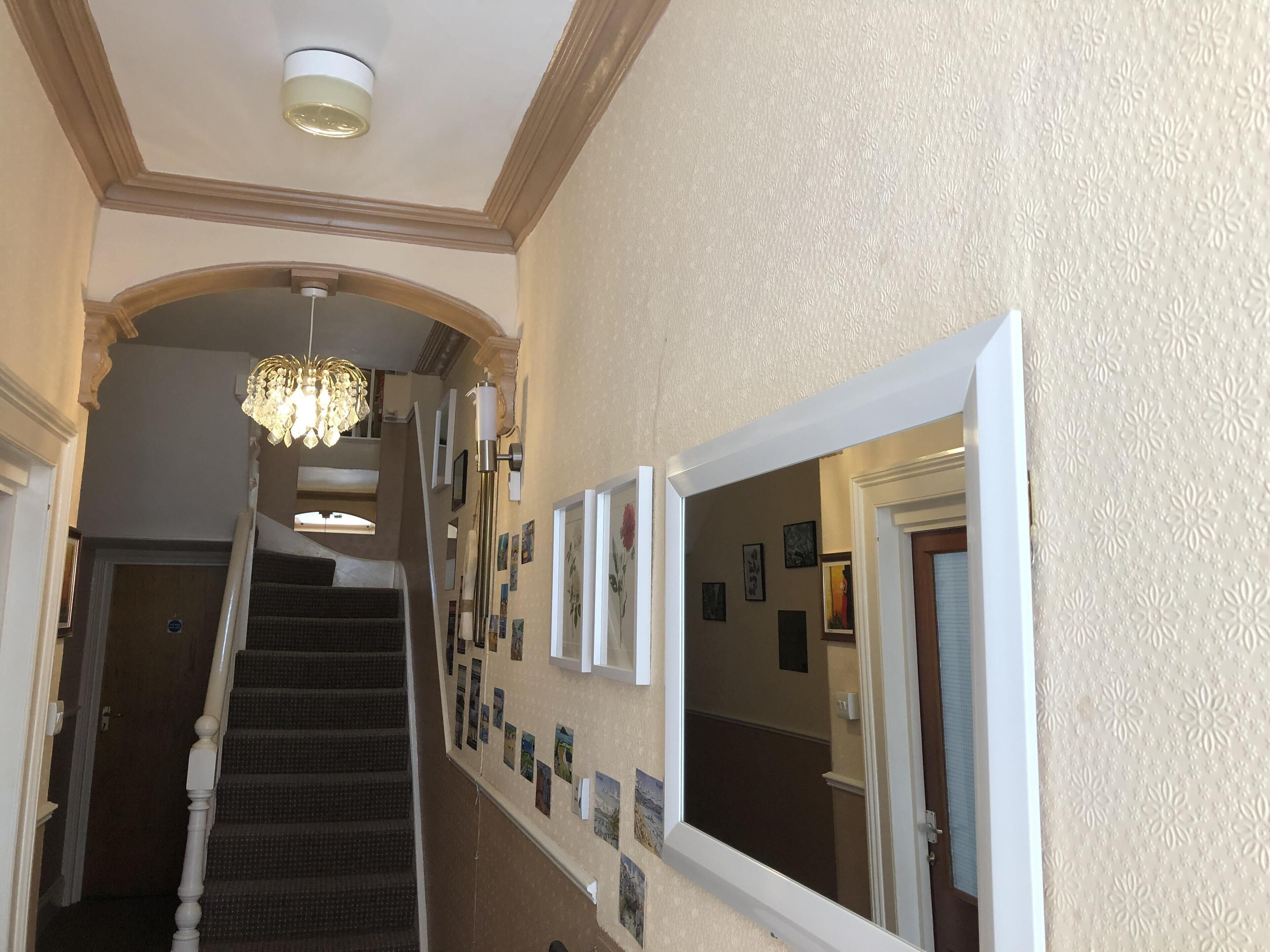 A hallway with a staircase, a chandelier, and framed pictures on the walls.