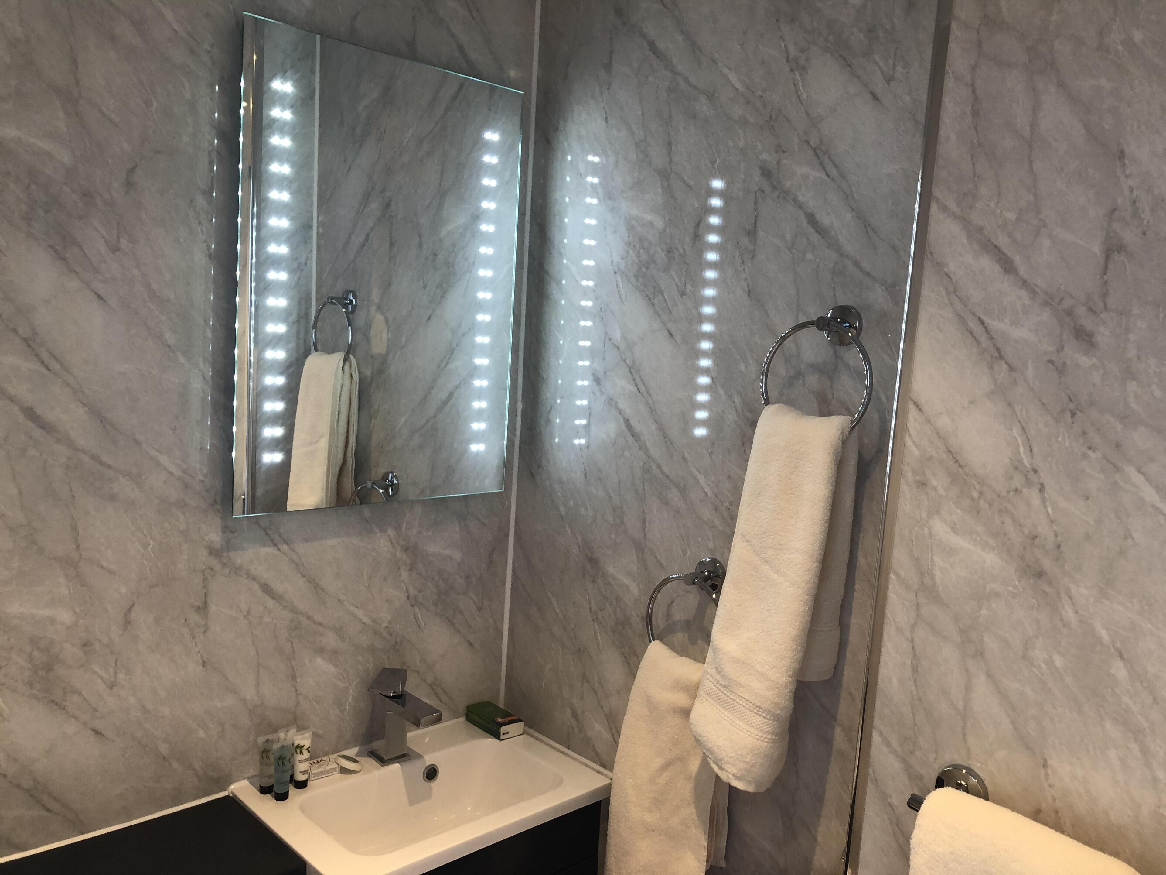 Um banheiro com parede de mármore, pia com espelho e duas toalhas penduradas em porta-toalhas.
