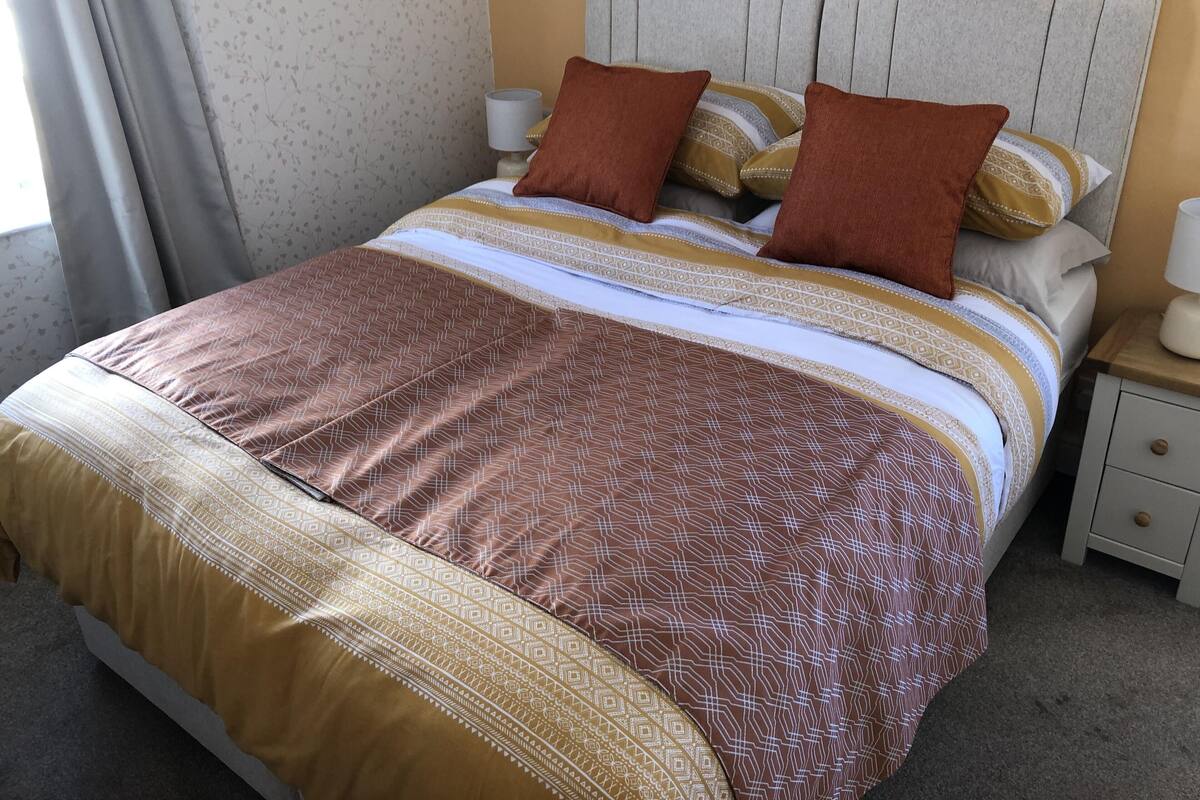 A neatly made bed with patterned bedding, a bedside table with a lamp, and a nightstand with a drawer.