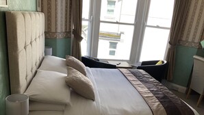 A neatly made bed with a headboard, a bedside table with a lamp, and a chair. - Harbour Lodge B&B (Paignton)