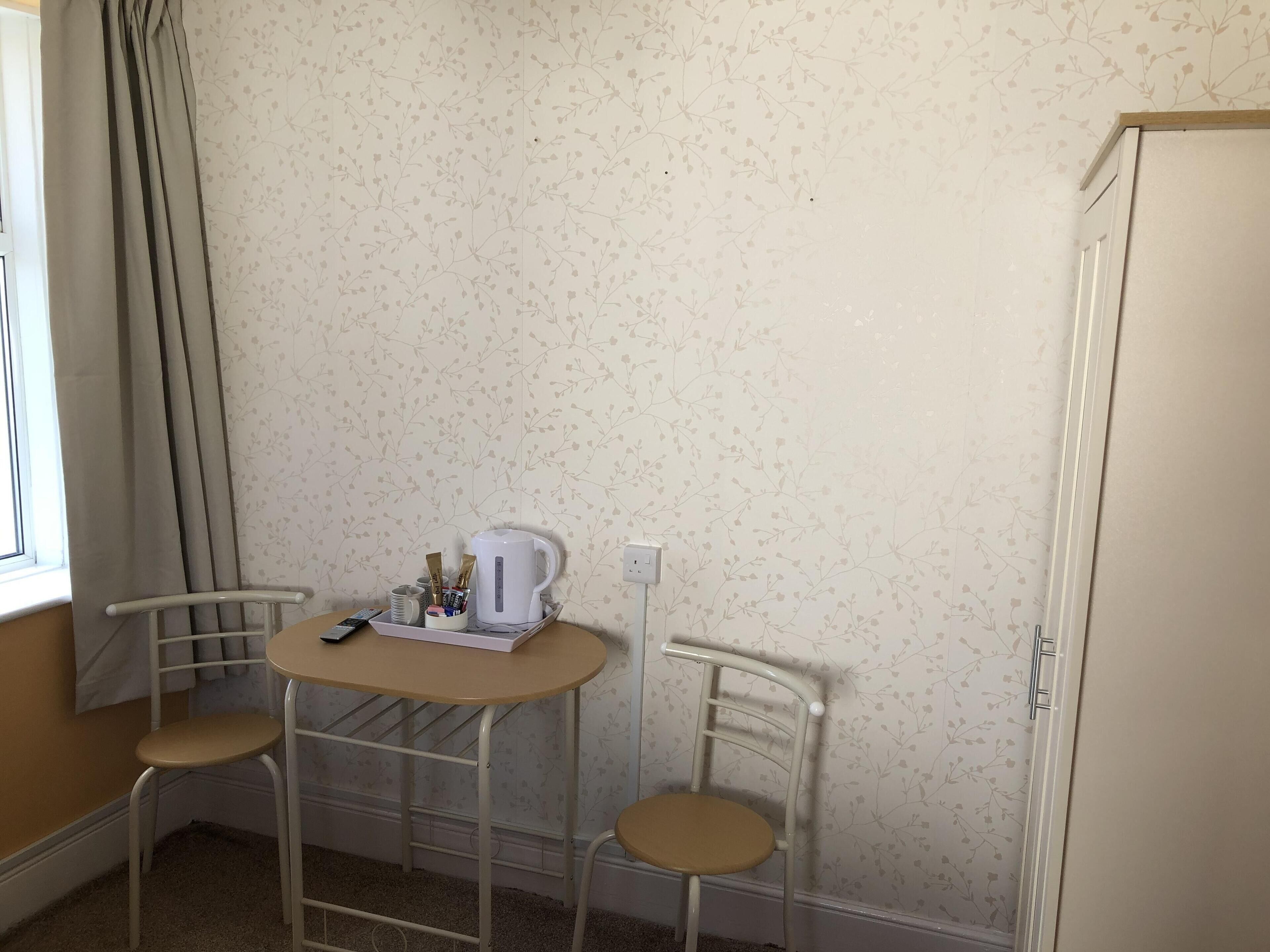 A small room with a single table, two chairs, a kettle, and a cabinet.