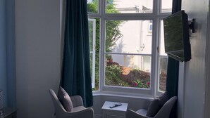 A corner room with a bay window, two chairs, a small table, and a TV mounted on the wall. - Harbour Lodge B&B (Paignton)