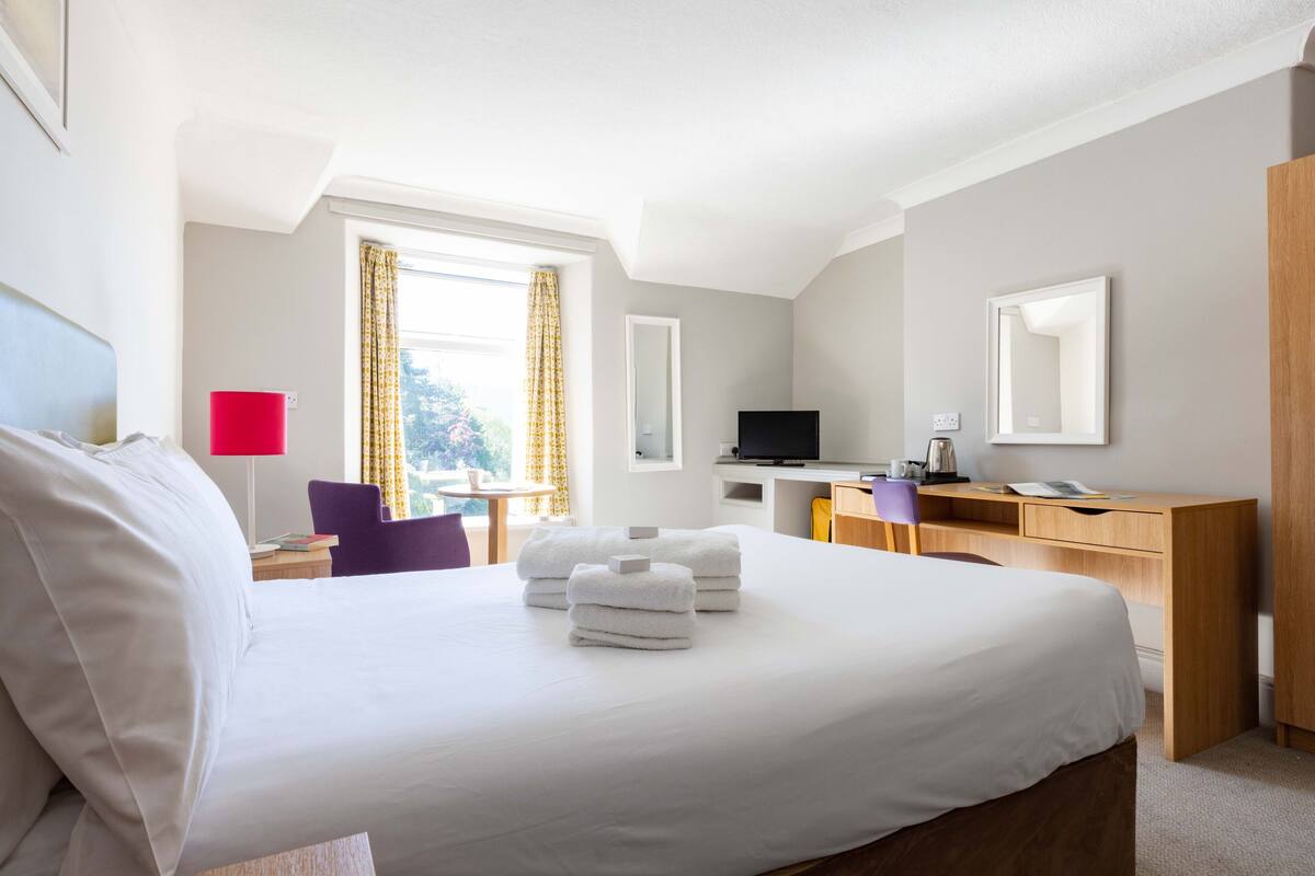 A hotel room with a bed, a desk, a chair, a TV, and a wardrobe.
