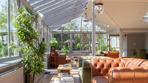 A conservatory with a glass ceiling, leather sofas, and a dining table with books and cups. - The Derwentwater Hotel (Keswick)