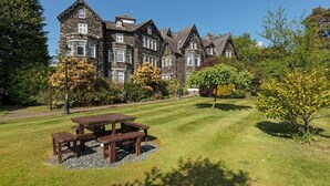 A large stone building with multiple windows and a lawn with a picnic table. - The Derwentwater Hotel (Keswick)