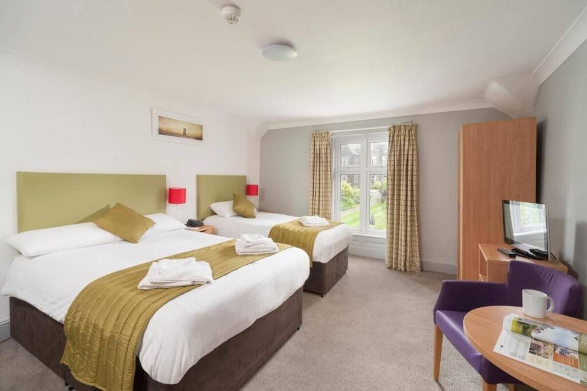 A hotel room with two beds, a TV, a desk, and a window with curtains.