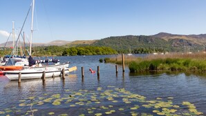 A calm lake with boats docked, surrounded by lush greenery and hills. - The Derwentwater Hotel (Keswick)