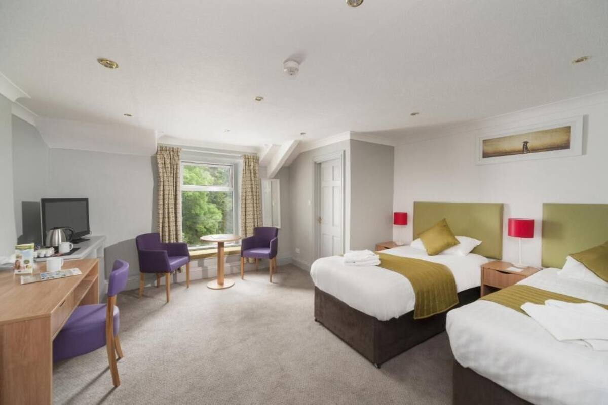 A hotel room with a bed, a desk, a chair, a television, and a window with curtains.