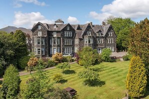 Um edifício de pedra grande e histórico com vários telhados apena e um gramado bem cuidado em primeiro plano.