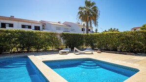 Une piscine divisée en deux zones distinctes, entourée d’une haie et bordée d’un bâtiment dont le toit est recouvert de tuiles.