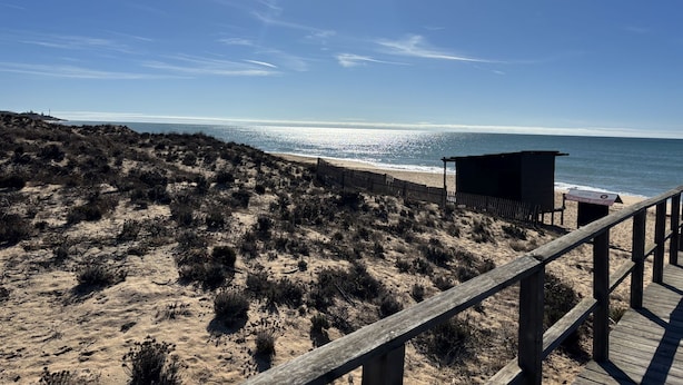 Une plage avec une promenade en bois qui mène à une petite construction en bois.