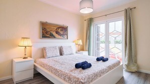 Une chambre à coucher avec un lit, deux tables de chevet, des lampes, un tableau et une fenêtre avec des rideaux.