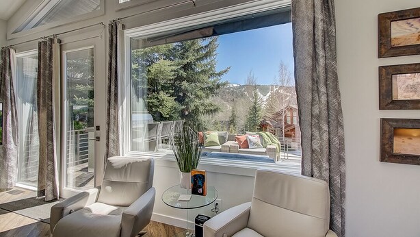 Un salón moderno con una mesa de vidrio, dos sillas, una planta en maceta y vistas a un balcón con mobiliario exterior.
