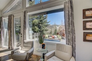 Un salón moderno con una mesa de vidrio, dos sillas, una planta en maceta y vistas a un balcón con mobiliario exterior.