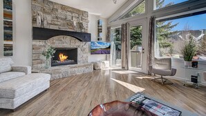 Una sala de estar moderna con chimenea de piedra, un sofá cómodo y un amplio ventanal con vistas al exterior.