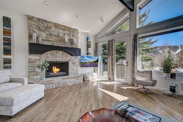 Una sala de estar moderna con chimenea de piedra, un sofá cómodo y un amplio ventanal con vistas al exterior.