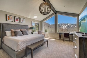 Un dormitorio con una cama grande, un escritorio y vistas a las montañas a través de amplias ventanas.