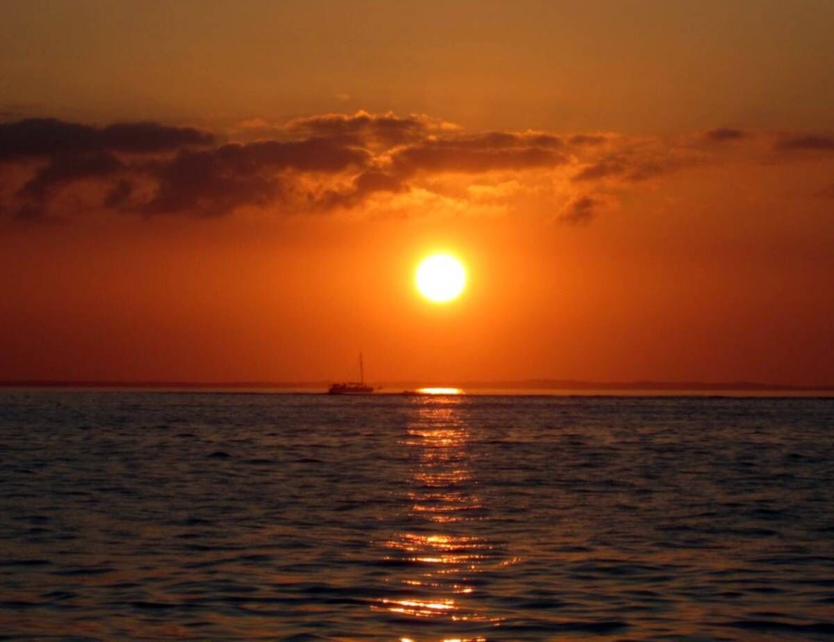 Un atardecer sobre el océano con un barco a lo lejos.