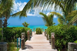 A wooden pathway leading to a beach with palm trees and a clear blue sky. - Villa Renaissance  Unit 501 1BR Pool/Garden (Grace Bay)