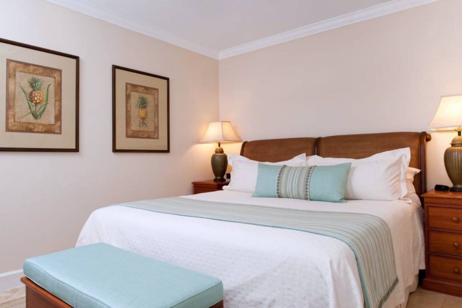 A neatly arranged bedroom with a bed, bedside tables, and two framed botanical prints on the wall.