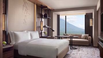A hotel room with a large bed, a sofa, a small table, a TV, a bookshelf, and a view of a mountain.