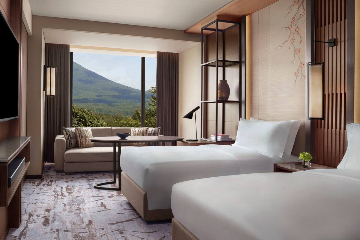 A hotel room with two beds, a sofa, a small table, and a TV.