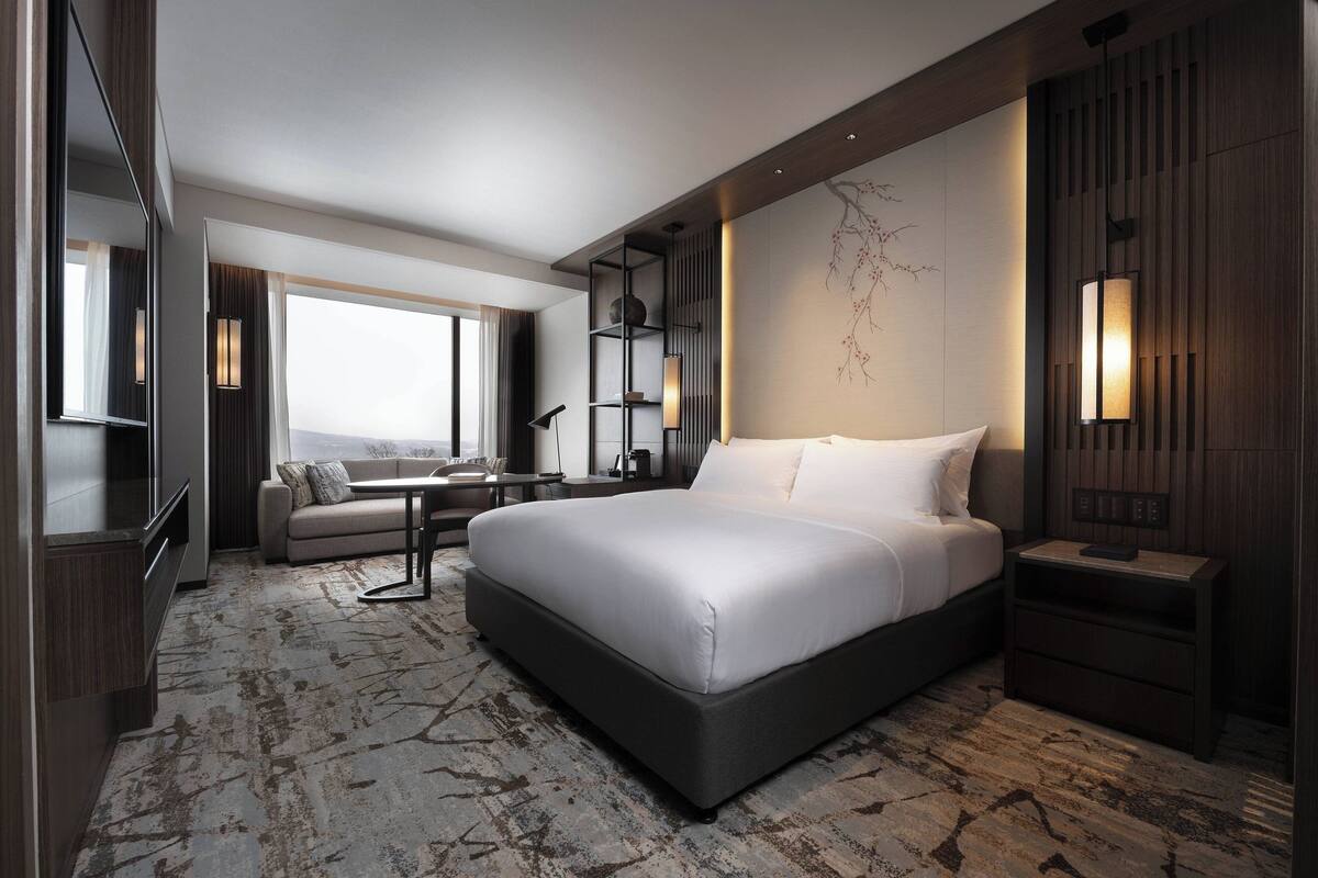 A modern hotel room with a large bed, a sofa, a desk, and a TV.