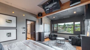 Moderni hotellihuone, jossa on suuri sänky, oleskelualue pyöreällä pöydällä sekä seinälle asennettu televisio.