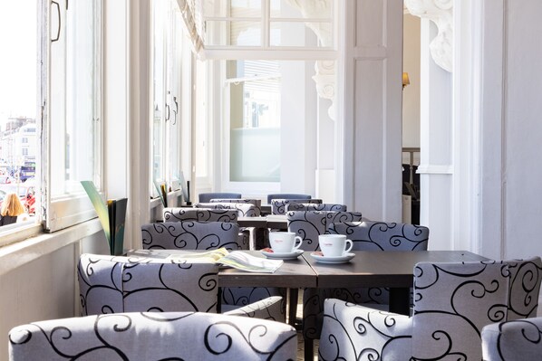 A café with patterned chairs and tables, a window with curtains, and a view of the street outside.