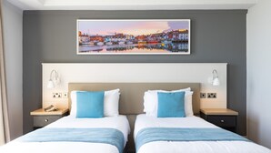 A hotel room with two beds, a large cityscape painting above the beds, and bedside lamps. - The Royal Hotel (Weymouth)