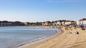 A beach with buildings in the background, sandy shore, and people enjoying the beach. - The Royal Hotel (Weymouth)