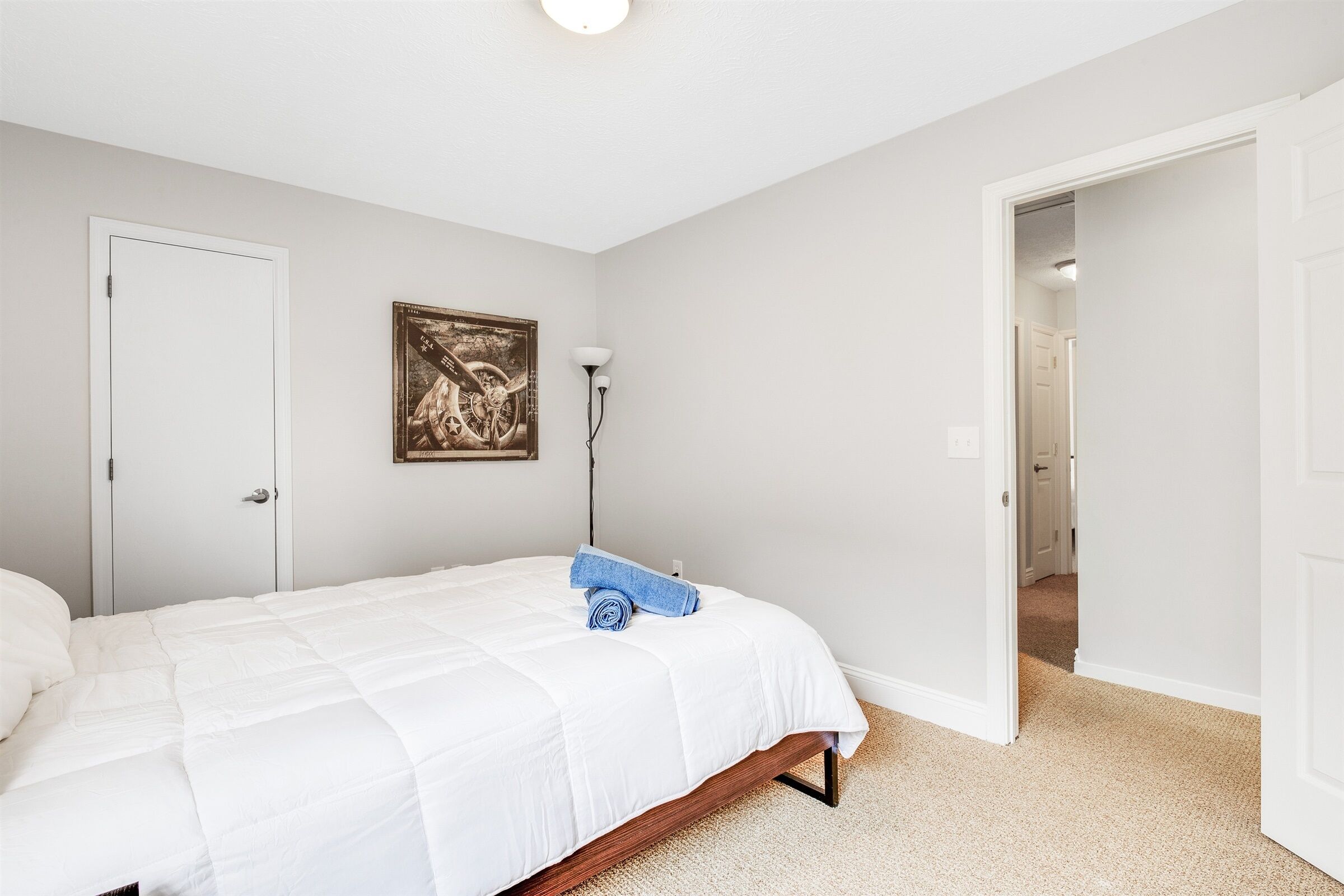 A bedroom with a bed, a door, a hallway, and a wall-mounted lamp.