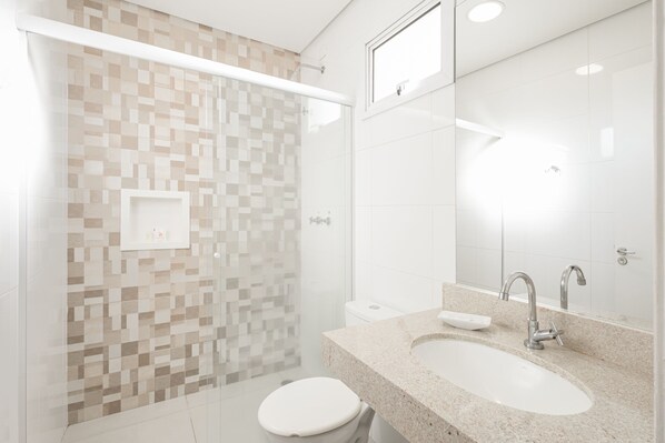 A modern bathroom with a glass shower enclosure, a white toilet, a sink with a mirror, and a tiled wall. - Sumaré Park Hotel (Sumare)