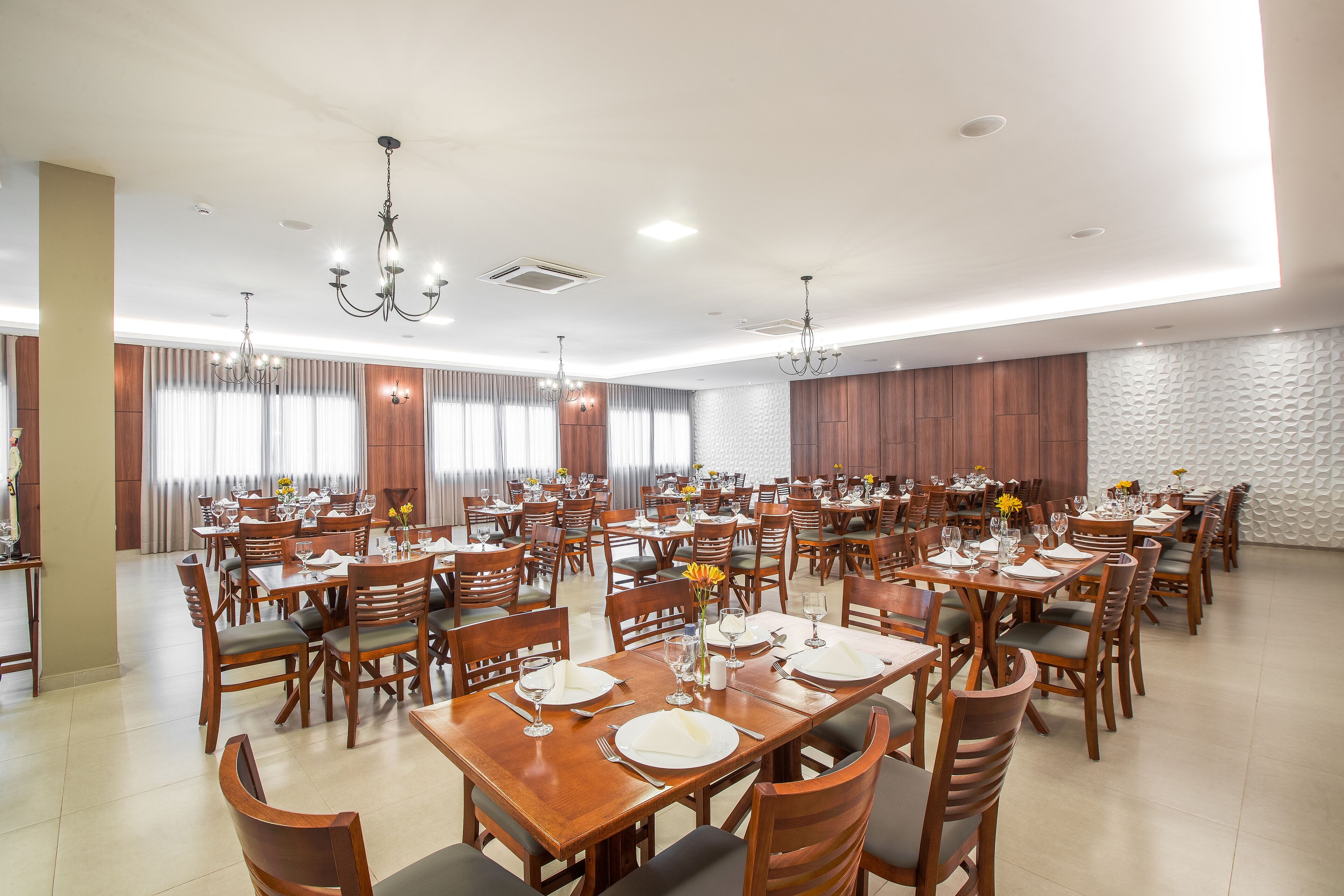 Une grande salle à manger avec de nombreuses tables et chaises, des lambris en bois sur les murs et des lustres.