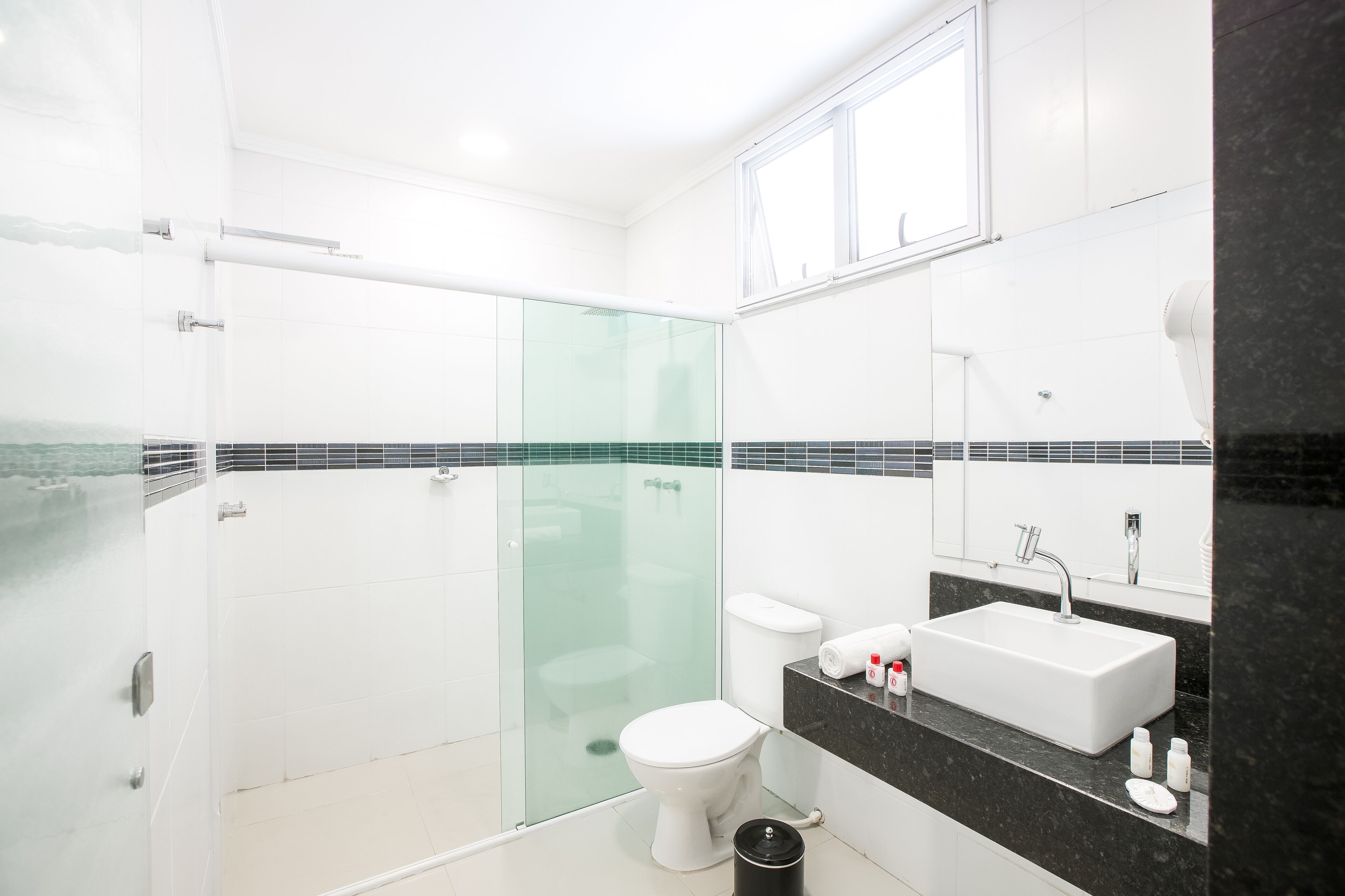 Un baño moderno con cabina de ducha de vidrio, inodoro blanco, encimera negra con lavabo y un espejo grande.